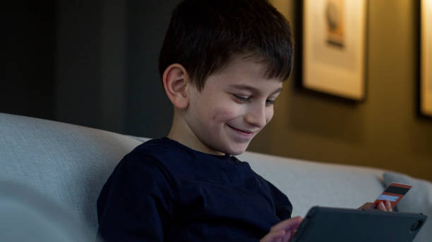 istock A young boy sits on a couch, engrossed in his tablet while holding a credit card, engaging in online shopping. Modern childhood, digital interaction, and tech-savvy youth in a cozy home 2165565148