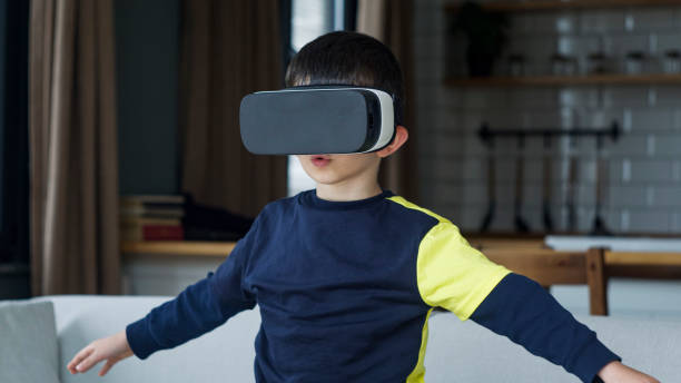 istock A young boy is immersed in a virtual reality experience, wearing VR and extending his arms as if interacting with a virtual environment. 2165565296