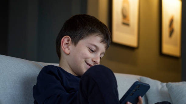 istock A young boy sits on a couch, happily engaged in a video conference call on smartphone. His smile and playful gesture capture the joy of connecting virtually. 2165565467