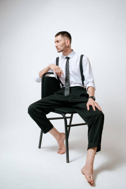 istock A man with white shirt and tie sits on a chair in studio. Barefoot 2165567065