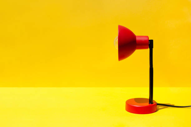 istock Red lamp on table in room with copy space. A red lamp on a bright yellow background. Minimal office or school equipment 2165567362