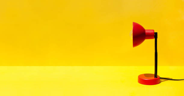 istock Red lamp on table in room with copy space. A red lamp on a bright yellow background. Minimal office or school equipment 2165567363