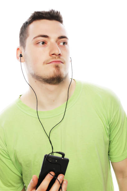 technology and people concept - young man wearing green t-shirt  listening music and using smartphone, isolated on white