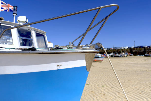 Close up of the white and blue bow of a fishing boat moored in low tide in St Ives Harbour, Cornwall, UK. In the near distance can be seen other moored fishing boats.