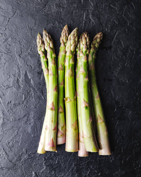 istock Top view of green asparagus sprouts on black background 2165583920