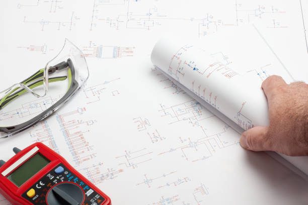 istock Electrical engineer reviewing schematics with multimeter and safety glasses. 2165588507