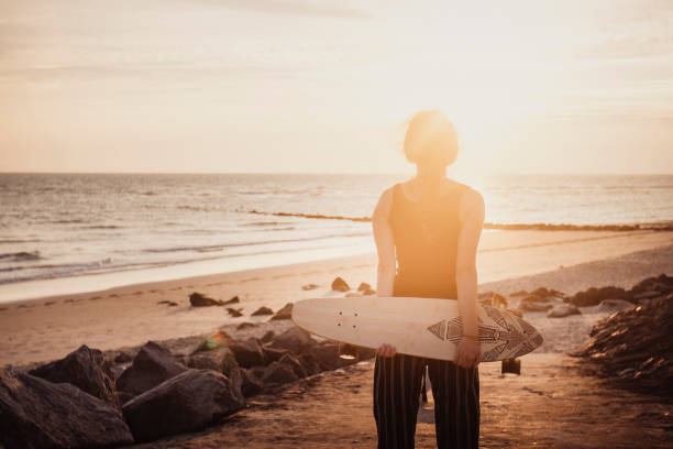 istock Young woman vacations at beach, holds skateboard 2165596167