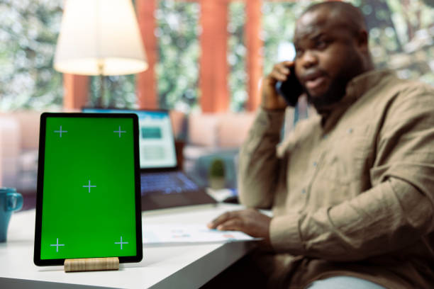 Business owner chats on phone call with shareholders next to green screen, transmitting data analytics sales reports from his home desk. Entrepreneur negotiates the funding with investors.