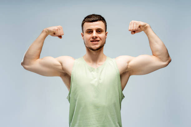 istock Athletic man flexing muscles showing biceps triceps on grey background looking at camera 2165597382