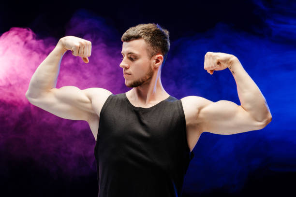 istock Serious, young athletic man showing muscles on colored smoke background 2165597413
