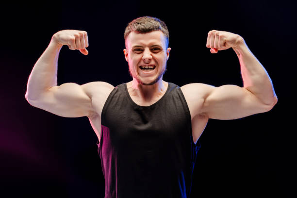 istock Bodybuilder man flexing muscles showing his strength, looking at camera isolated on black background 2165597419