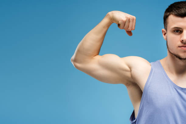istock Young athletic man showing biceps on blue background, copy space, isolated on blue background 2165597427