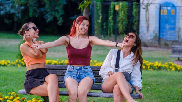 istock Three beautiful young women sitting on a bench in a park, chatting joyfully 2165604697