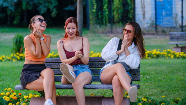 istock Three beautiful young women sitting on a bench in a park, chatting joyfully 2165604711