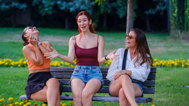 istock Three beautiful young women sitting on a bench in a park, chatting joyfully 2165604728