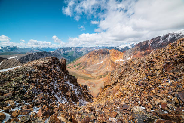 Top view from abyss edge between rocks to multicolor valley of iron colors and big sharp rocky ridge of red color. Colorful large mountains in freshly fallen snow in low clouds. Vivid alpine scenery. vista superior desde el borde del abismo entre rocas hasta el valle multicolor de colores de hierro y una gran cresta rocosa afilada de color rojo. grandes montañas coloridas en nieve recién caída en nubes bajas. vívidos paisajes alpinos.