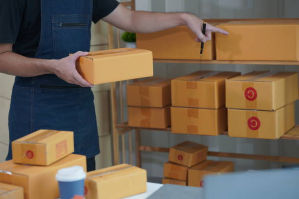 istock SME business Young man working with laptop with cardboard boxes stacked on table ready for delivery, indicating small business or home office. 2165610998