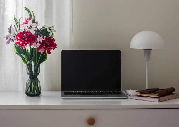 istock An open laptop, a bouquet of flowers, a table lamp, a notebook on a white table. Copy space 2165620131