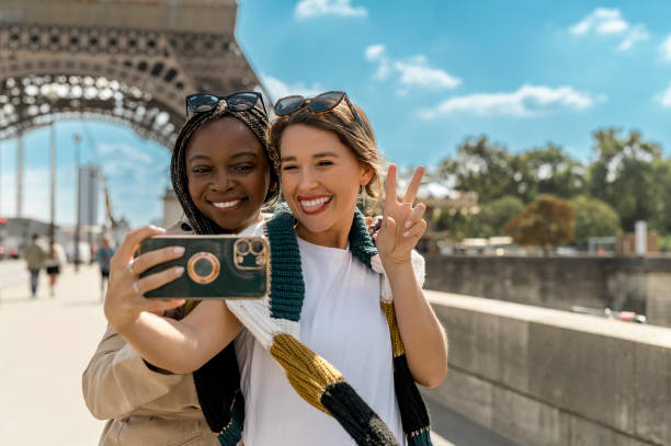 istock Young diverse girlfriends taking selfie, smiling cheekily at cellphone whilst sightseeing in Paris 2165626859