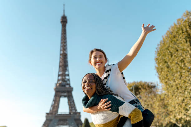 istock Low angle view of young multiethnic girlfriends raising arm, playing piggyback with Eiffel Tower in background 2165626866