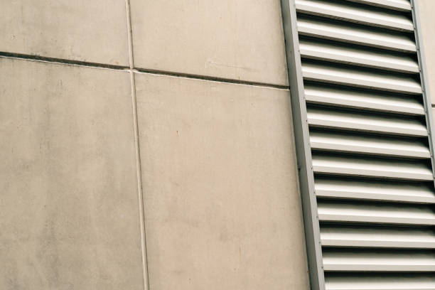 istock a concrete wall with a vertical metal louver panel running along its side. The concrete is smooth and light gray, while the louvers are silver and have a slightly textured finish. 2165635570