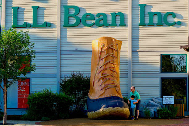 Freeport, Maine, USA - June 30, 2019: A man helps lift a boy onto the oversized, famous “L.L. Bean boot” in front of the company’s flagship store.