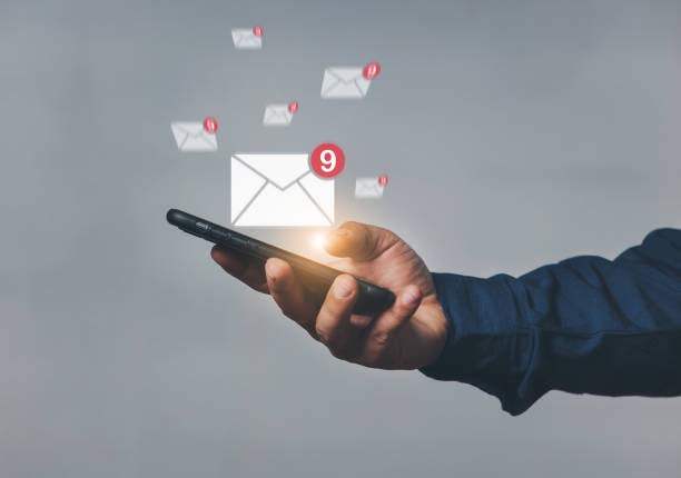 istock Hand-holding mobile phone with email icon on screen. Business communication technology concept. A human hand holds a phone while sending and receiving email from the internet. 2165640383
