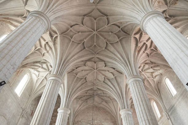 The image captures the stunning intricate details of a vaulted ceiling supported by grand stone columns inside a historic church. The architectural design showcases exquisite craftsmanship with its elaborate patterns and structural elegance. The high arches and symmetrical designs create a sense of awe and reverence, highlighting the historical and cultural significance of the building. The natural light streaming through the windows enhances the beauty of the stonework, emphasizing the grandeur and timelessness of this sacred space.