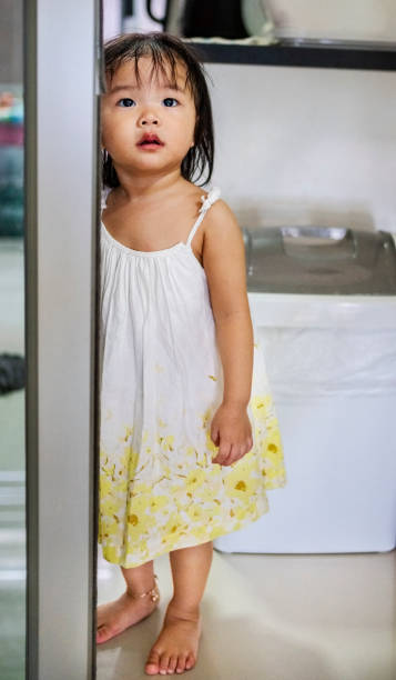 Innocent little girl standing by door and looking away at home