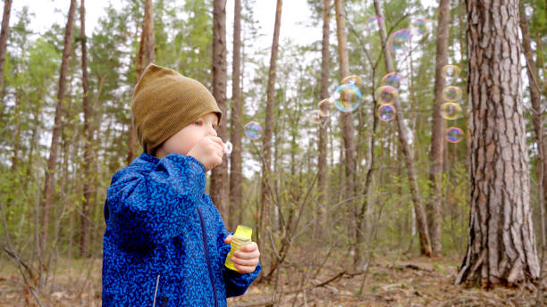 istock Happy playful boy blowing soap bubbles in the forest. 2165675062