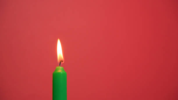 A green candle burning brightly against a vibrant red background, creating a warm and cozy atmosphere. Happy birthday or anniversary video in 4K resolution with copy space. Colorful festive background