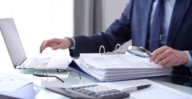 istock Businessman or auditor is looking through binders with papers while using a calculator and magnifying glass for financial documents analyzing. Audit and taxes concept 2165679167