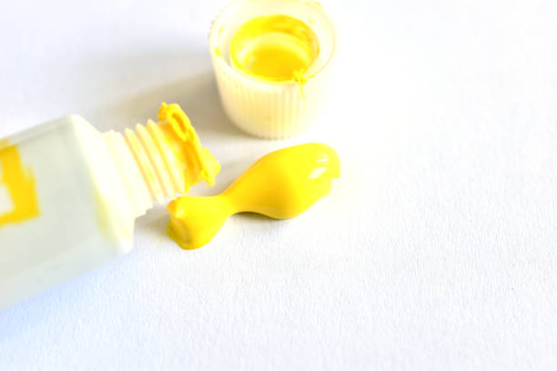 A tube of acrylic paint and a drop of yellow paint on a white background lies near the tube.