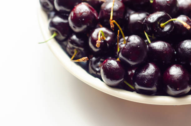 A bowl of cherries is shown on a white background. The cherries are ripe and ready to eat. The bowl is filled to the brim with cherries, and they are all different sizes