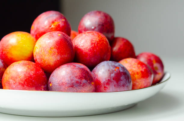 A white plate with a bunch of red plums on it. The plums are arranged in a way that they look like they are ready to be eaten. The plate is placed on a table, and the table is also white