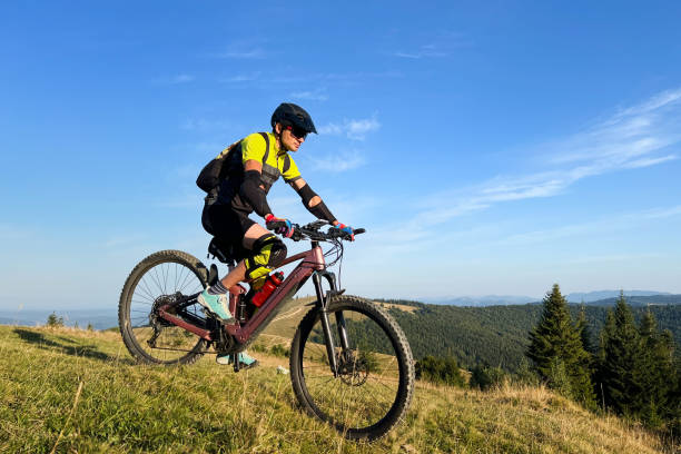 Cyclist man riding electric mountain bike outdoors along grassy trail in the mountains. stock photo