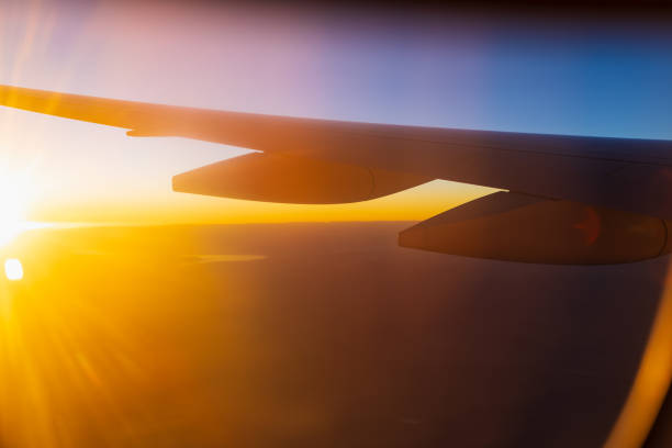 Golden sunlight rays against airplane wing silhouette background. Sunrise or sundown above the clouds. View from airplane window