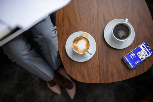 Unrecognizable businesswoman sitting in hotel room. On the table is smart phone with boarding pass on display and two cups of coffee.