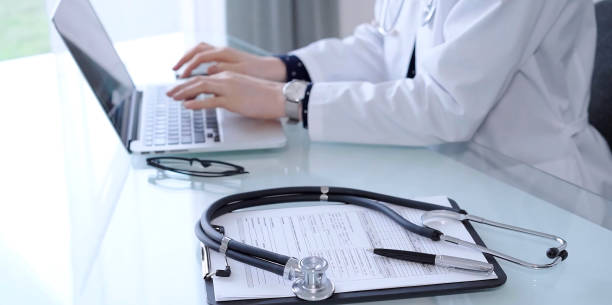 istock Stethoscope and medication history record form are lying on the glass table while doctor is working at the background. Medicine and healthcare 2165703829