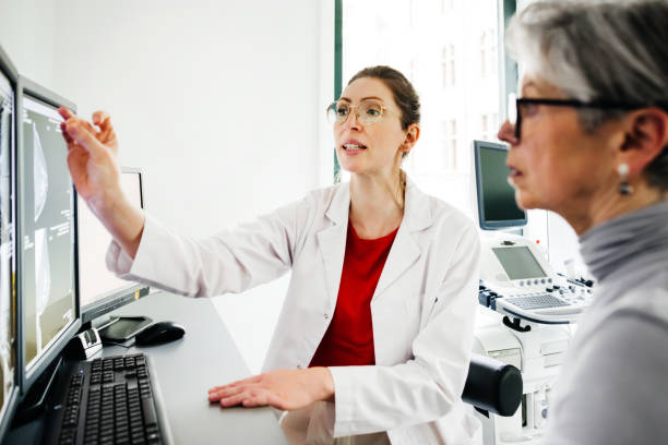Young Female Doctor Pointing at Computer Screen While Explaining to Senior Patient