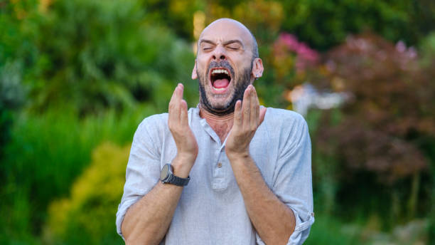 istock A middle-aged handsome businessman in a park, looking at the camera while sneezing 2165741771