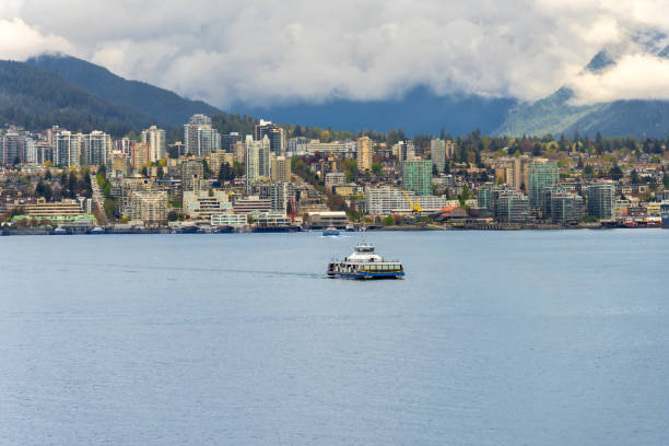 Vancouver, BC, Canada - April 26, 2024: A SeaBus passenger ferry boat traveling in Vancouver Harbour with North Vancouver in the background.
