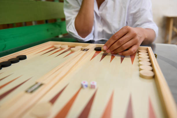 Close-up of a person playing backgammon outdoors. The image focuses on hand movements, game pieces, and the board. Perfect for representing strategy, leisure, and board games.