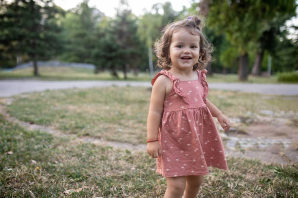 Portrait of beautiful smiling little girl with curly hair, in pink summer dress, in the public park.