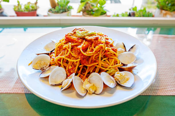 Spaghetti with clams in tomato sauce on white plate.