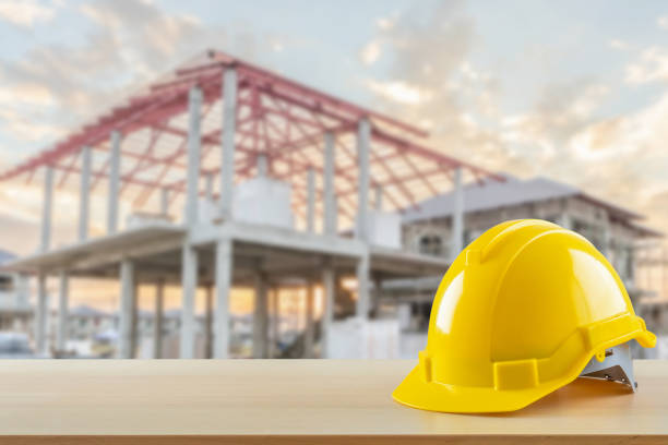 istock Yellow safety construction helmet on wood table with construction site background 2165789234