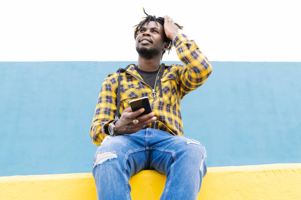 istock black man sitting on a wall with a phone at hand 2165789884
