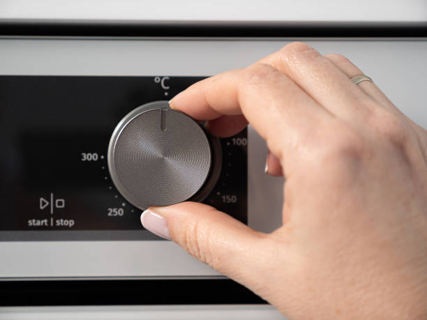 istock Woman adjusting modern white oven in kitchen.  Female hand pushing and turning knobs on oven control panel 2165790415