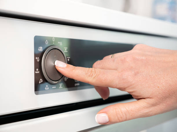 istock Woman adjusting modern white oven in kitchen.  Female hand pushing and turning knobs on oven control panel 2165791516