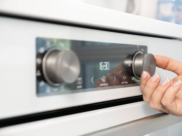 istock Woman adjusting modern white oven in kitchen.  Female hand pushing and turning knobs on oven control panel 2165791854